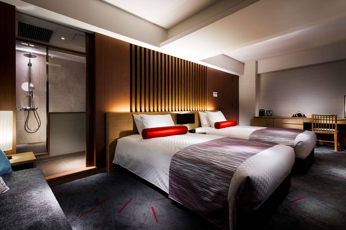 Une chambre d’hôtel moderne équipée de deux lits, d’une douche, d’un bureau et d’une télévision.