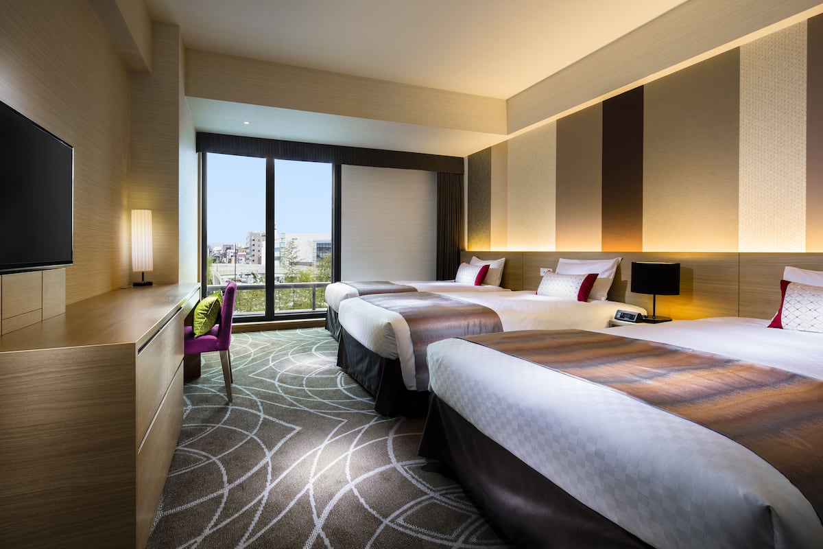 Une chambre d’hôtel avec deux lits, une télévision, un bureau et une vue sur la ville.