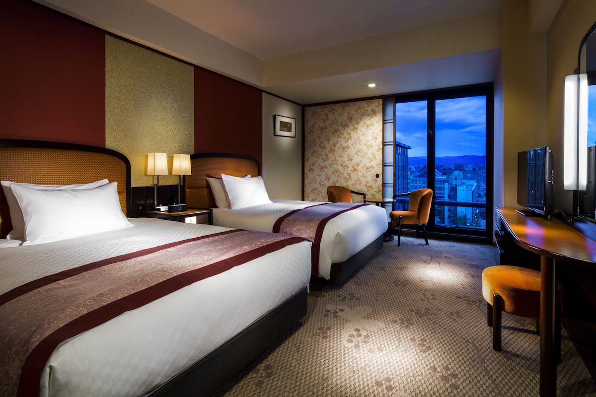 Une chambre d’hôtel avec deux lits, un bureau, une chaise et un téléviseur.