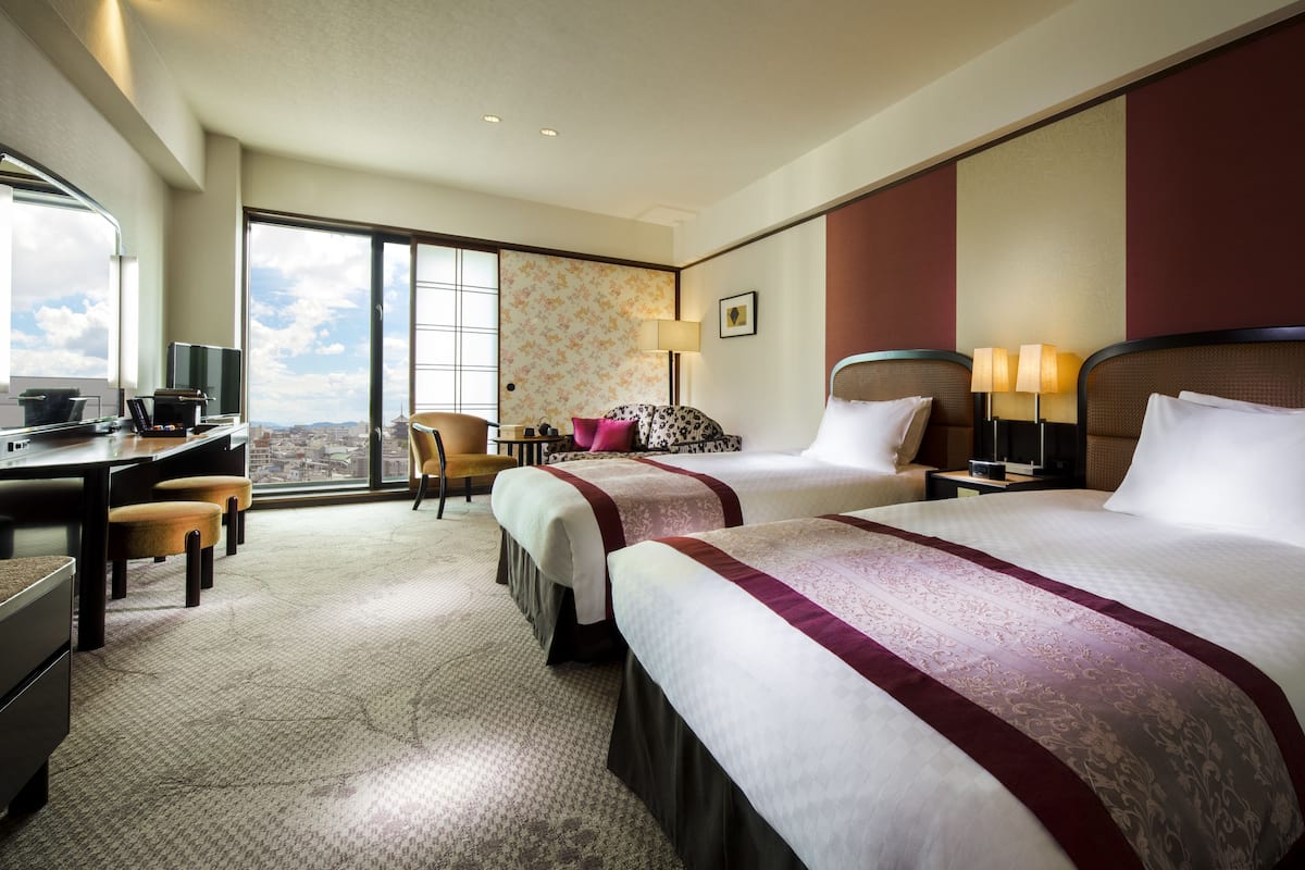 Une chambre d’hôtel avec deux lits, un bureau, une chaise et une vue sur la ville.