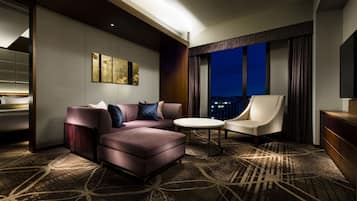 A modern hotel room with a sectional sofa, a round table, and a single armchair.