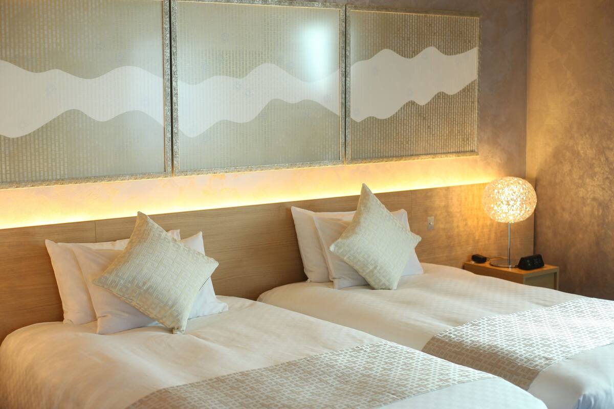 Une chambre d’hôtel avec deux lits, une table de chevet avec une lampe et un mur au décor texturé.