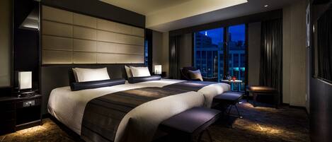 A modern hotel room with a large bed, a seating area, and a view of the cityscape.
