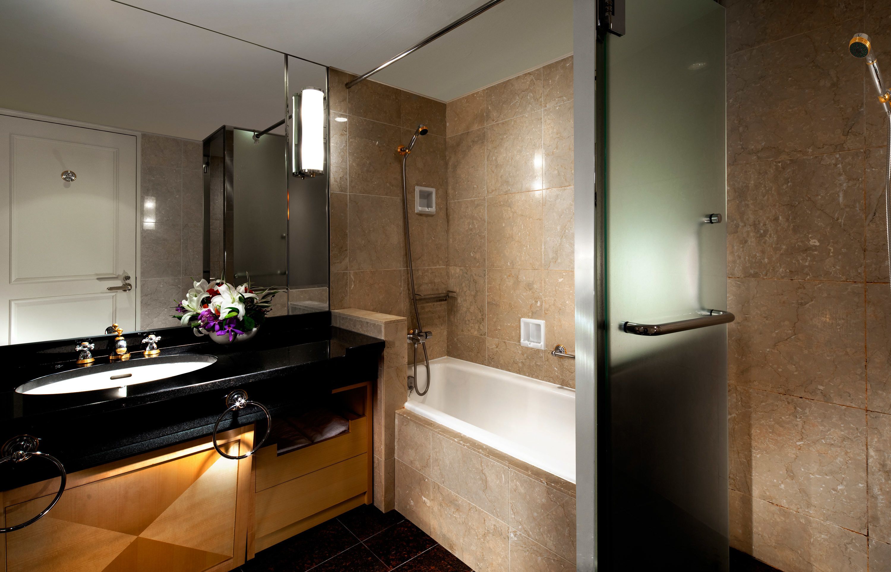 Un bagno moderno con lavabo su piano nero, cabina doccia in vetro e pareti rivestite di piastrelle color crema.