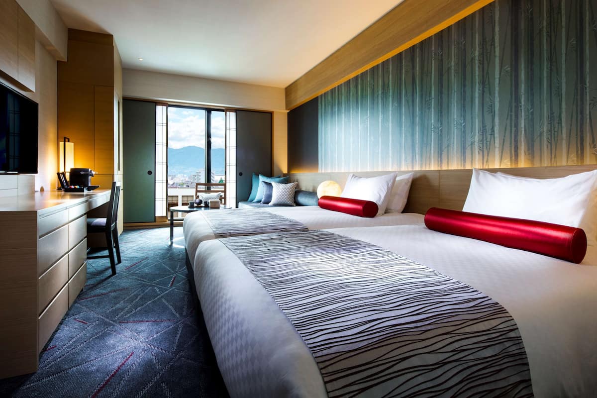 Une chambre d’hôtel avec un grand lit, un bureau avec une machine à café, une chaise et une vue sur la ville grâce à de grandes fenêtres.