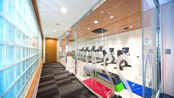 A modern fitness center with exercise equipment, a glass wall, and a patterned carpet.