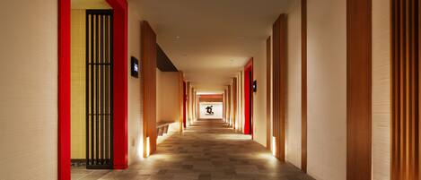 Un largo y estrecho pasillo de hotel con piso a cuadros, paneles de madera en las paredes y una pared roja decorativa a la izquierda.