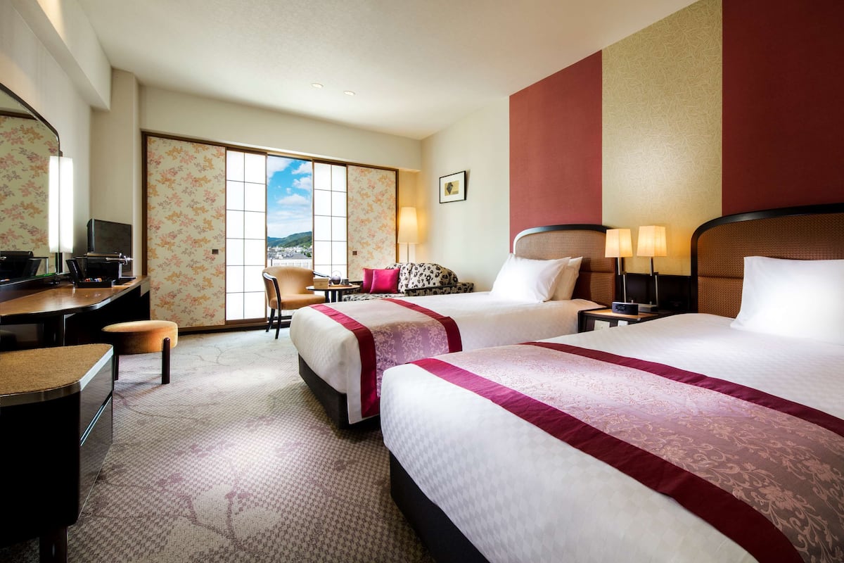 Une chambre d’hôtel avec deux lits, un bureau, une chaise et une télévision.