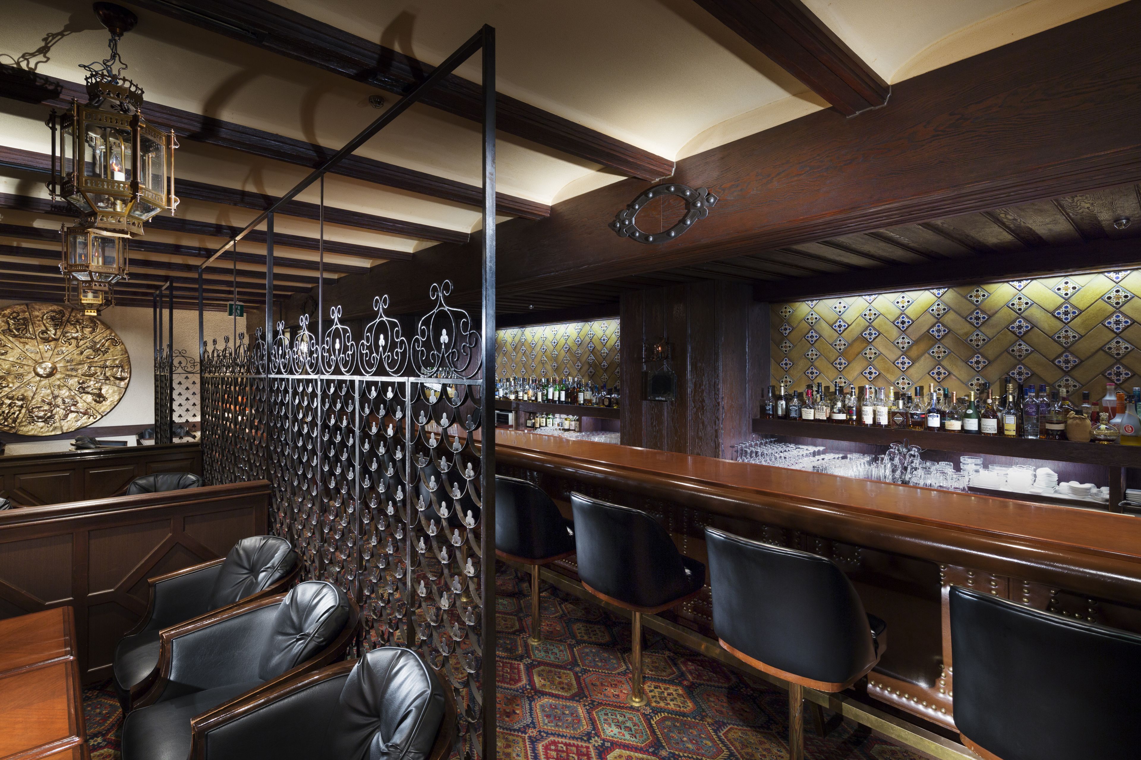 A bar area with wooden beams, a patterned wall, and a variety of bottles.