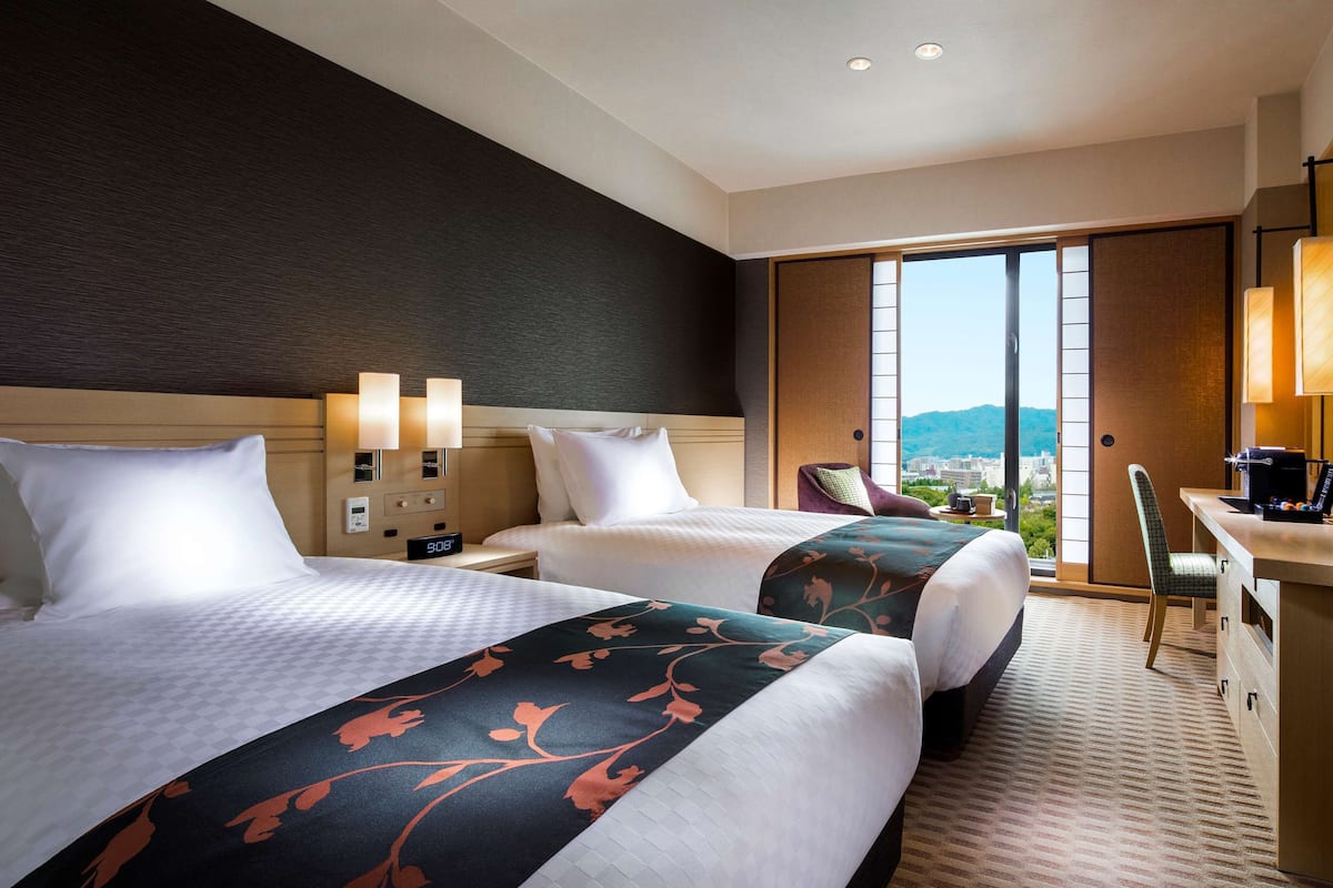 Une chambre d’hôtel avec deux lits, un bureau et une vue sur la ville.