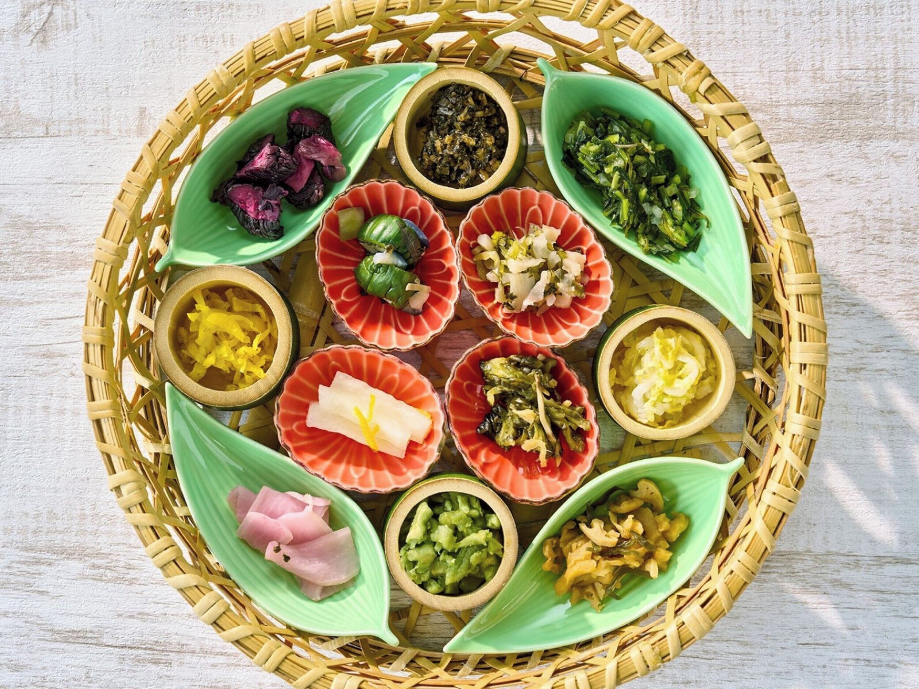Una cesta redonda tejida que contiene varios alimentos en platos con forma de hojas verdes y rojas.