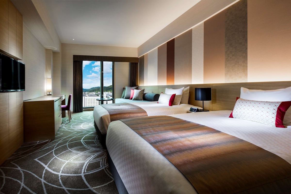 Une chambre d’hôtel avec deux lits, un bureau, une télévision et une grande fenêtre donnant sur la ville.