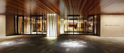 Un moderno vestíbulo de hotel con techo de listones de madera, puertas de cristal y piso de baldosas.