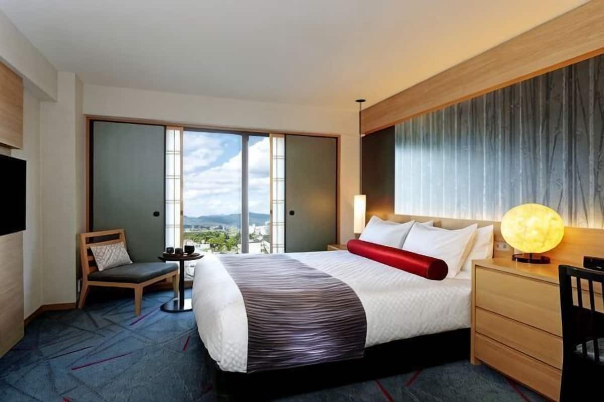 Une chambre d’hôtel avec un lit, une chaise, un bureau, une lampe et une vue par la fenêtre.