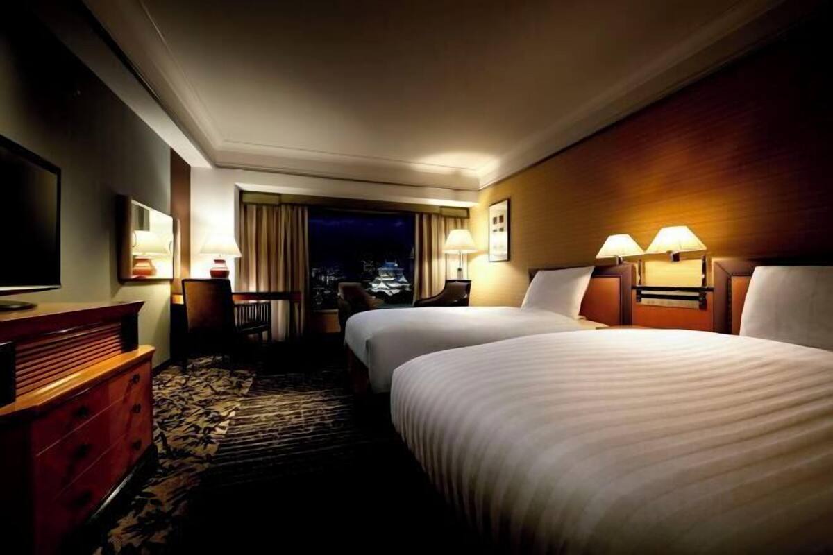 Camera d'albergo con due letti, televisione, comò e vista sulla città di notte.