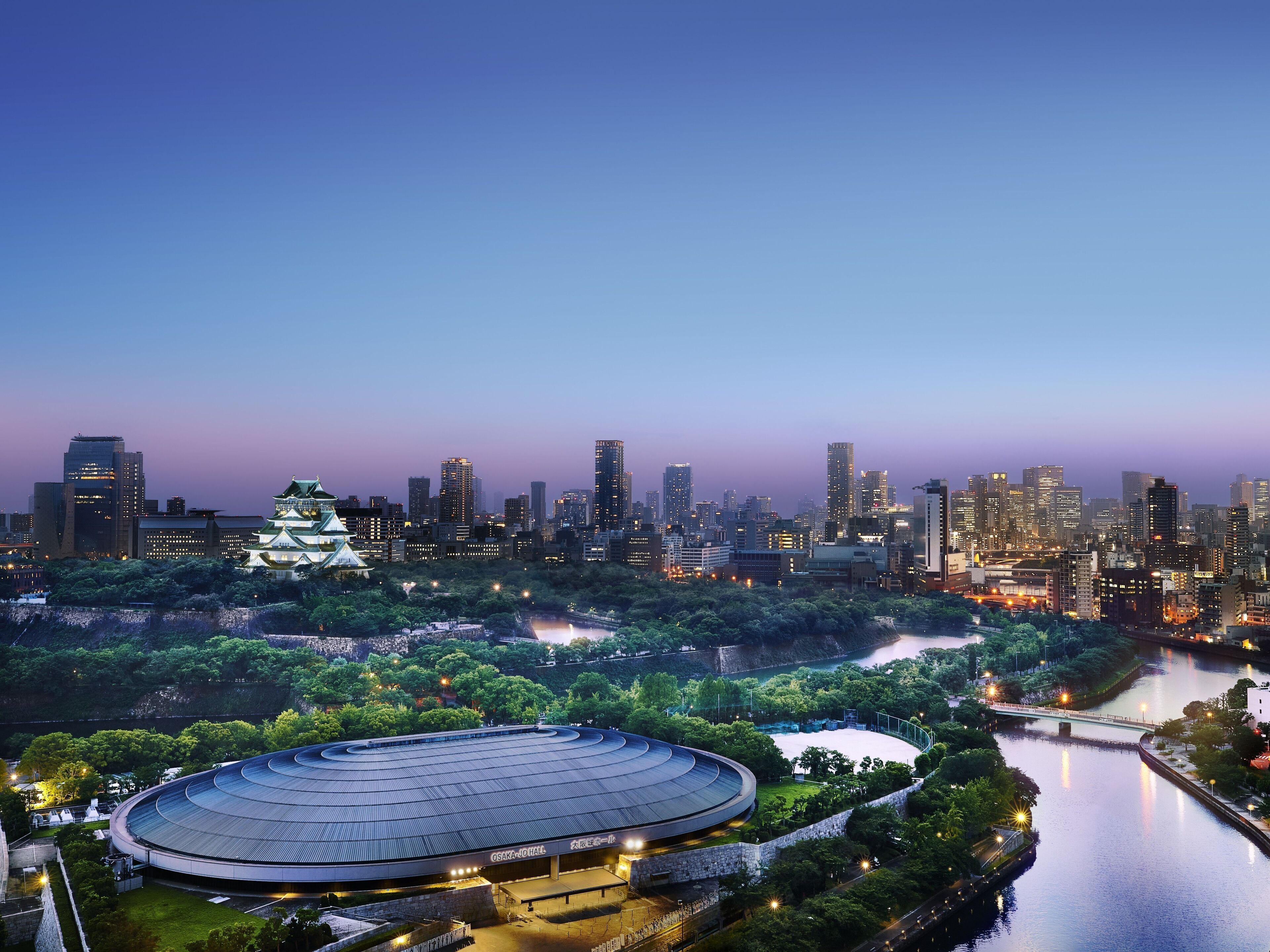 Une vue urbaine avec un imposant édifice ressemblant à un château, une rivière et un grand stade.