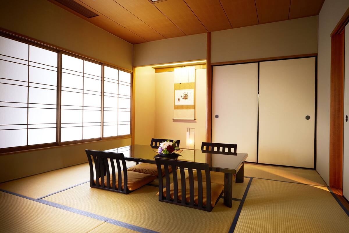 Una tradizionale stanza giapponese con pavimento in tatami, un tavolino con un vaso di fiori e porte scorrevoli.