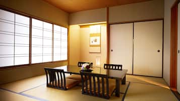 A traditional Japanese room with tatami flooring, a low table with a vase of flowers, and sliding doors.