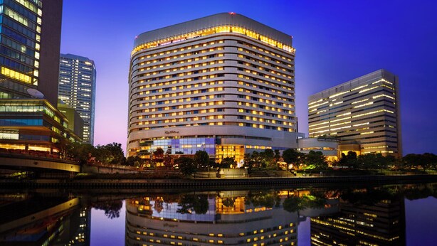 A multi-story hotel with a curved facade, large windows, and a reflection in a body of water.