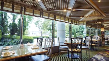 Un restaurante con mesas y sillas dispuestas para comer, grandes ventanales que ofrecen vistas a zonas verdes.