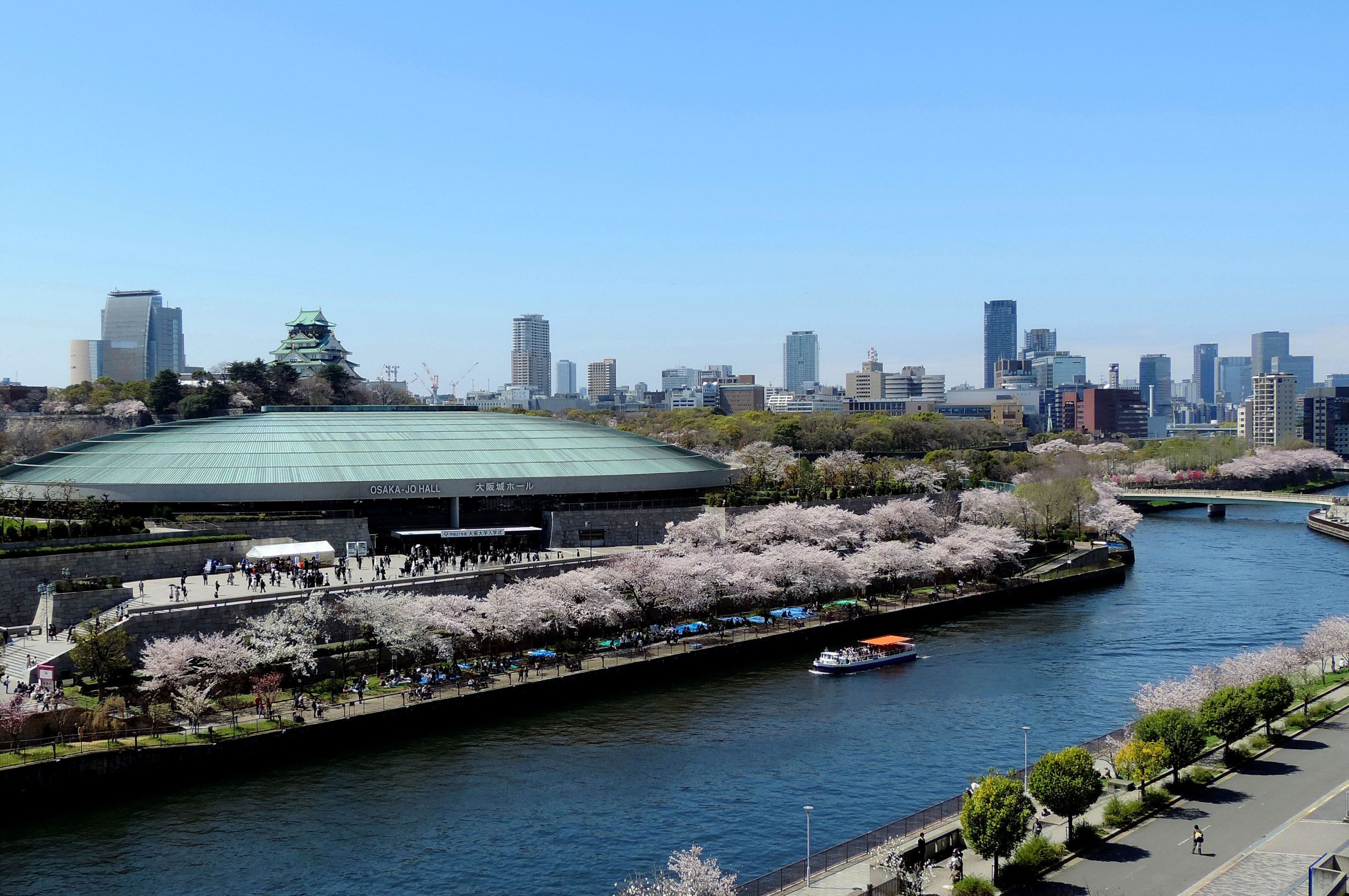A riverside view with a large stadium, cherry blossoms, and a city skyline.