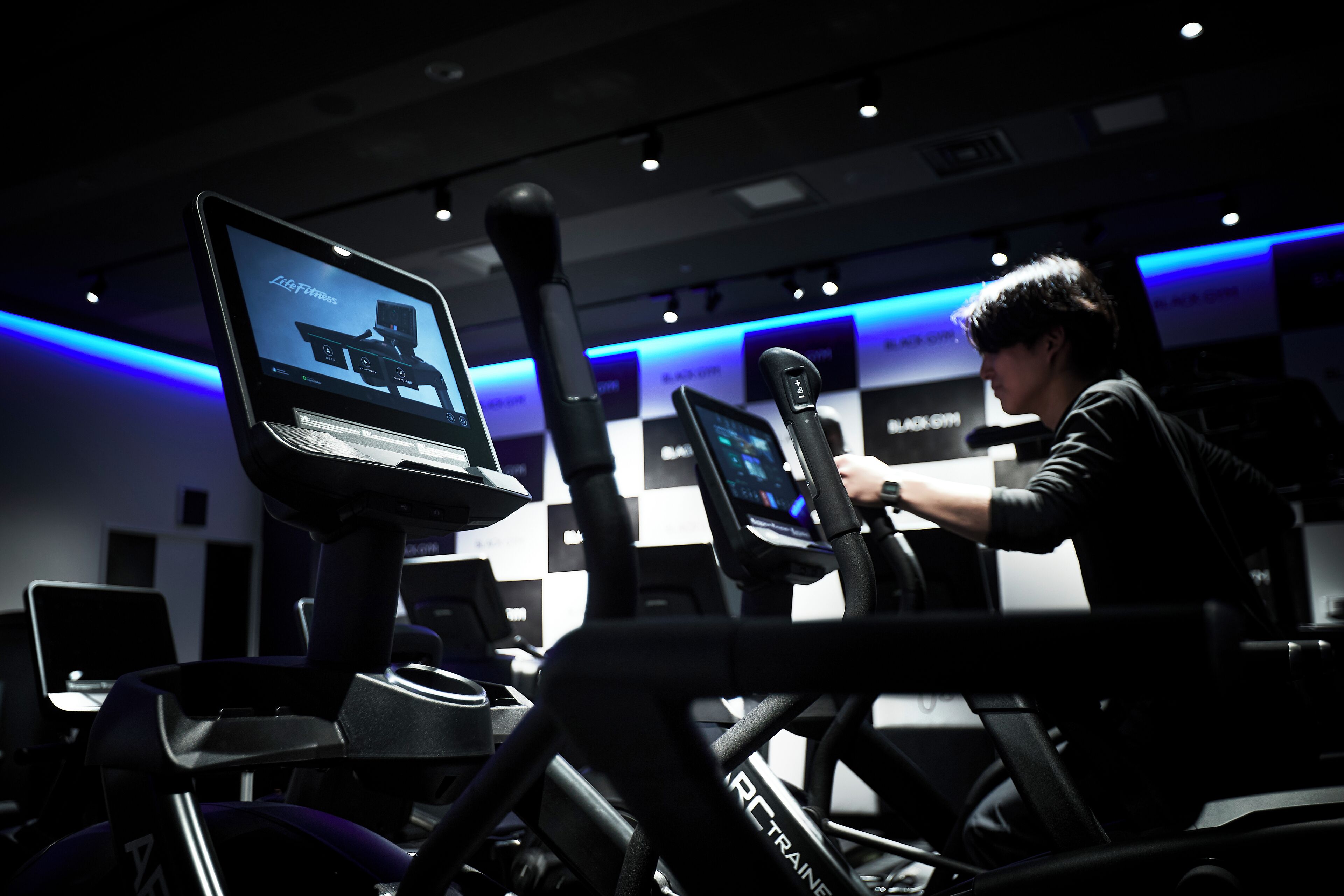 A gym with treadmills and exercise equipment, a digital display, and a person using a treadmill.