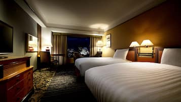 A hotel room with two beds, a desk, a chair, and a view of the city at night.