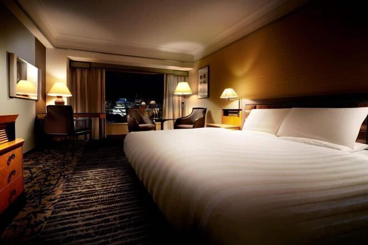 Camera d'albergo con un letto grande, una scrivania, due sedie, un comodino e vista sulla città.