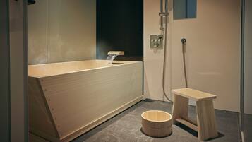 A modern bathroom with a wooden bathtub, a small wooden stool, and a shower area.