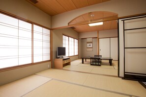 A traditional Japanese room with tatami flooring, a television, a low table with chairs, and sliding doors.