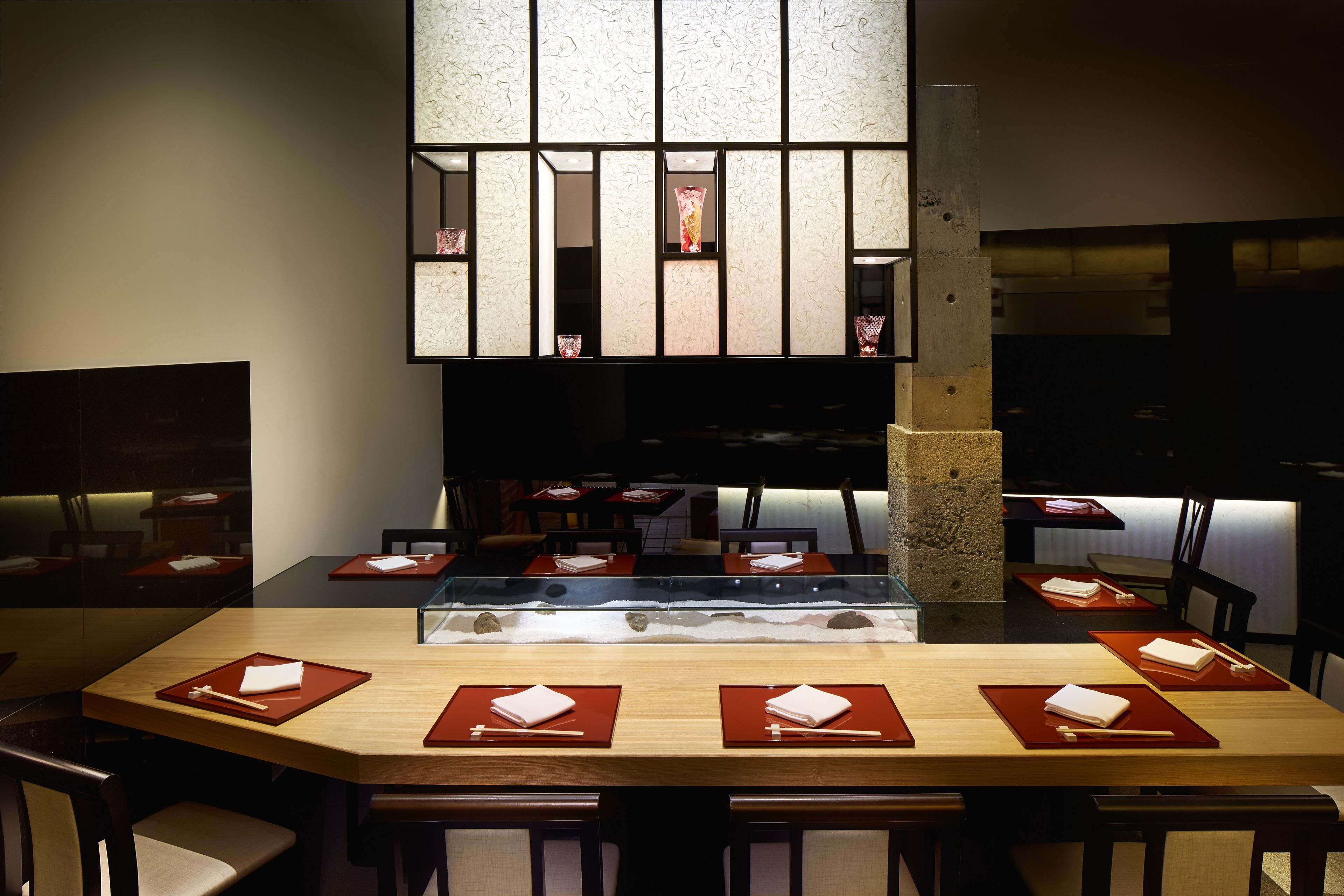 Un restaurante con una larga mesa de madera dispuesta para varios comensales, con individuales rojos y palillos.