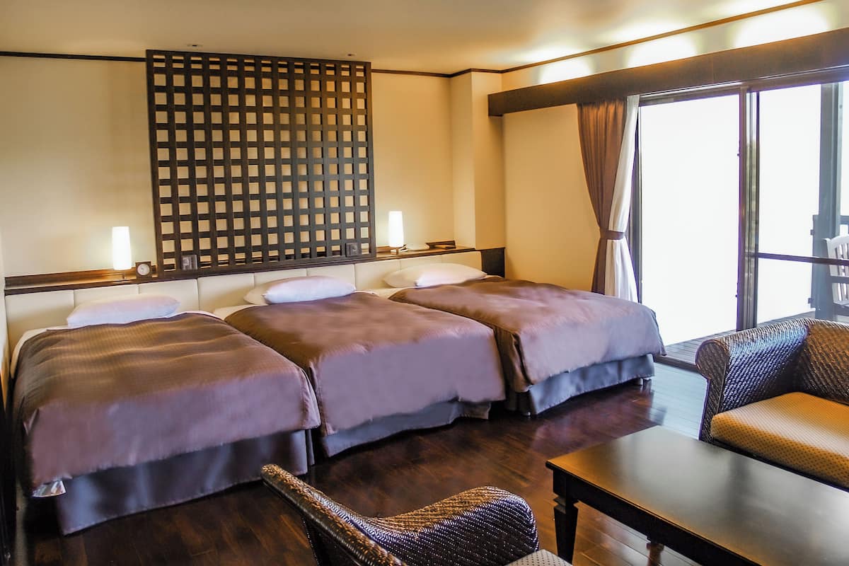 A hotel room with two beds, a sofa, a table, and a large window.
