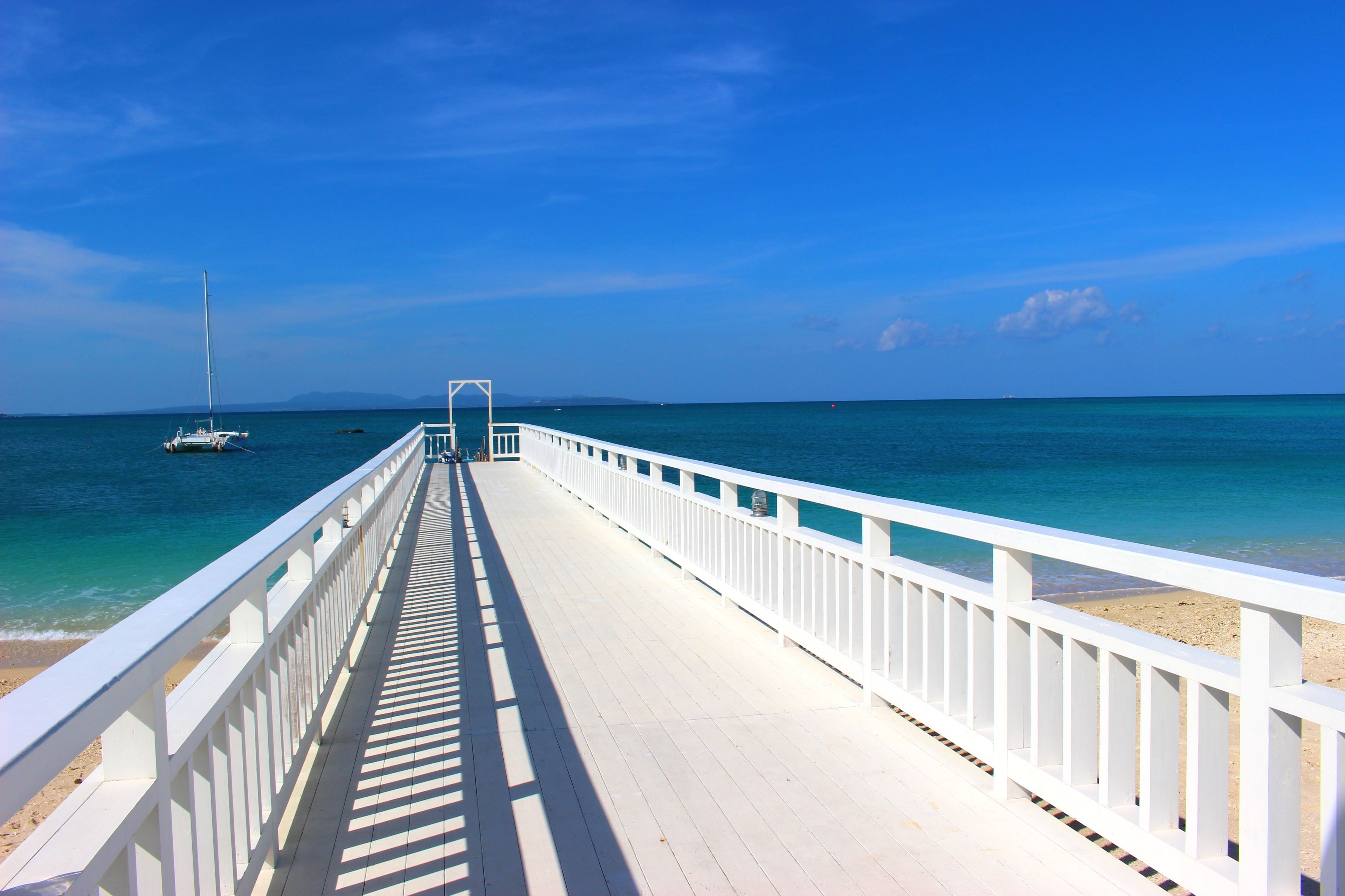 A white pier extending into a calm sea with a clear sky.