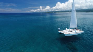 A sailboat on a clear blue sea with a distant landmass and clouds.