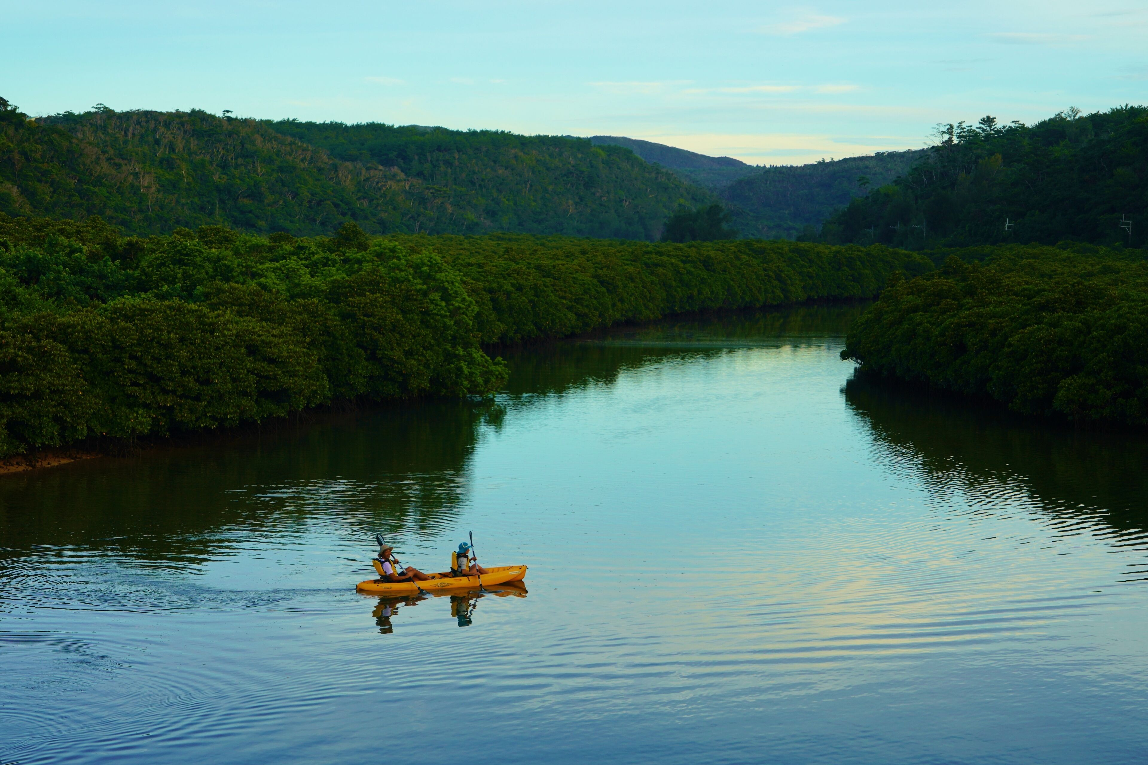 A calm river with a kayak in the middle.