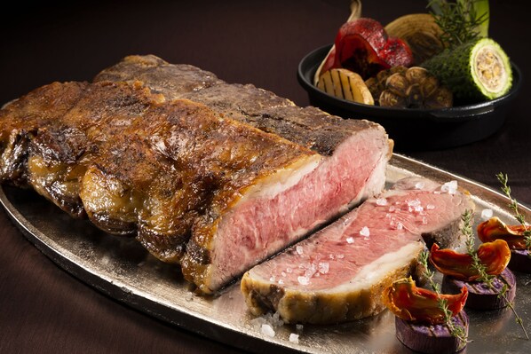 A large steak with a slice cut out, garnished with herbs and vegetables on a metal plate.