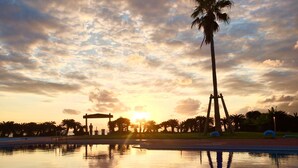 Un coucher de soleil paisible sur une piscine bordée de palmiers, avec une pancarte indiquant « ORION BEACH ».
