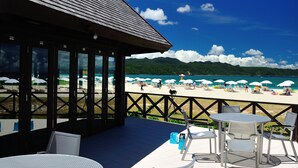 Une terrasse au bord de la plage, avec des sièges extérieurs et une vue sur la plage et les montagnes.