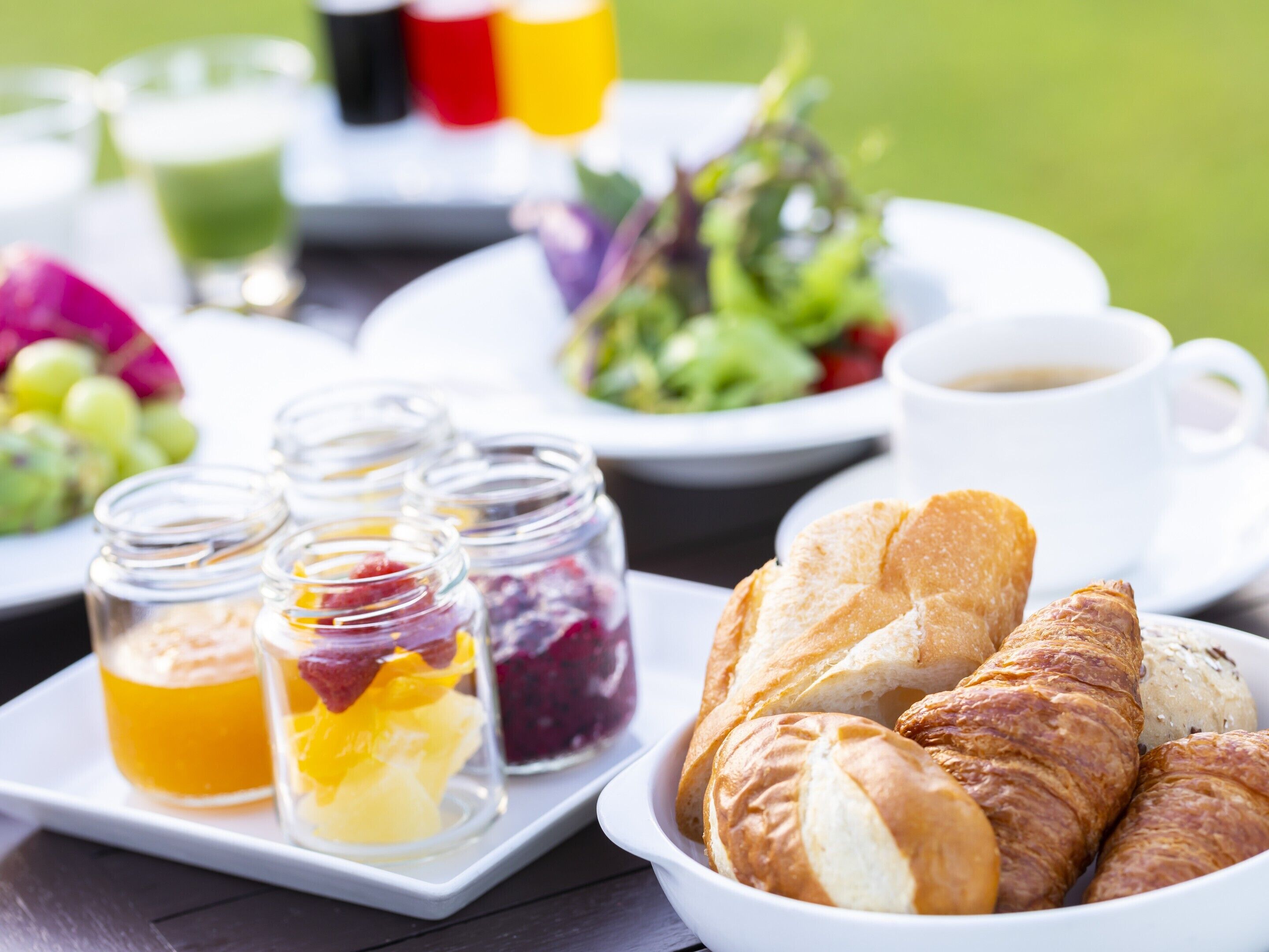 A breakfast setting with croissants, fruit preserves, and a cup of coffee on a white plate.