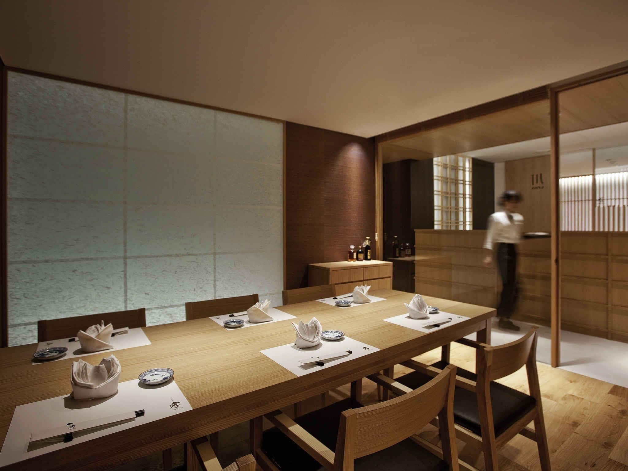 Un comedor moderno con una larga mesa de madera, sillas y una persona al fondo.