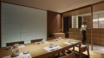 Un comedor moderno con una larga mesa de madera, sillas y una persona al fondo.