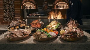 Diversas carnes y verduras sobre una encimera, con un cocinero al fondo.