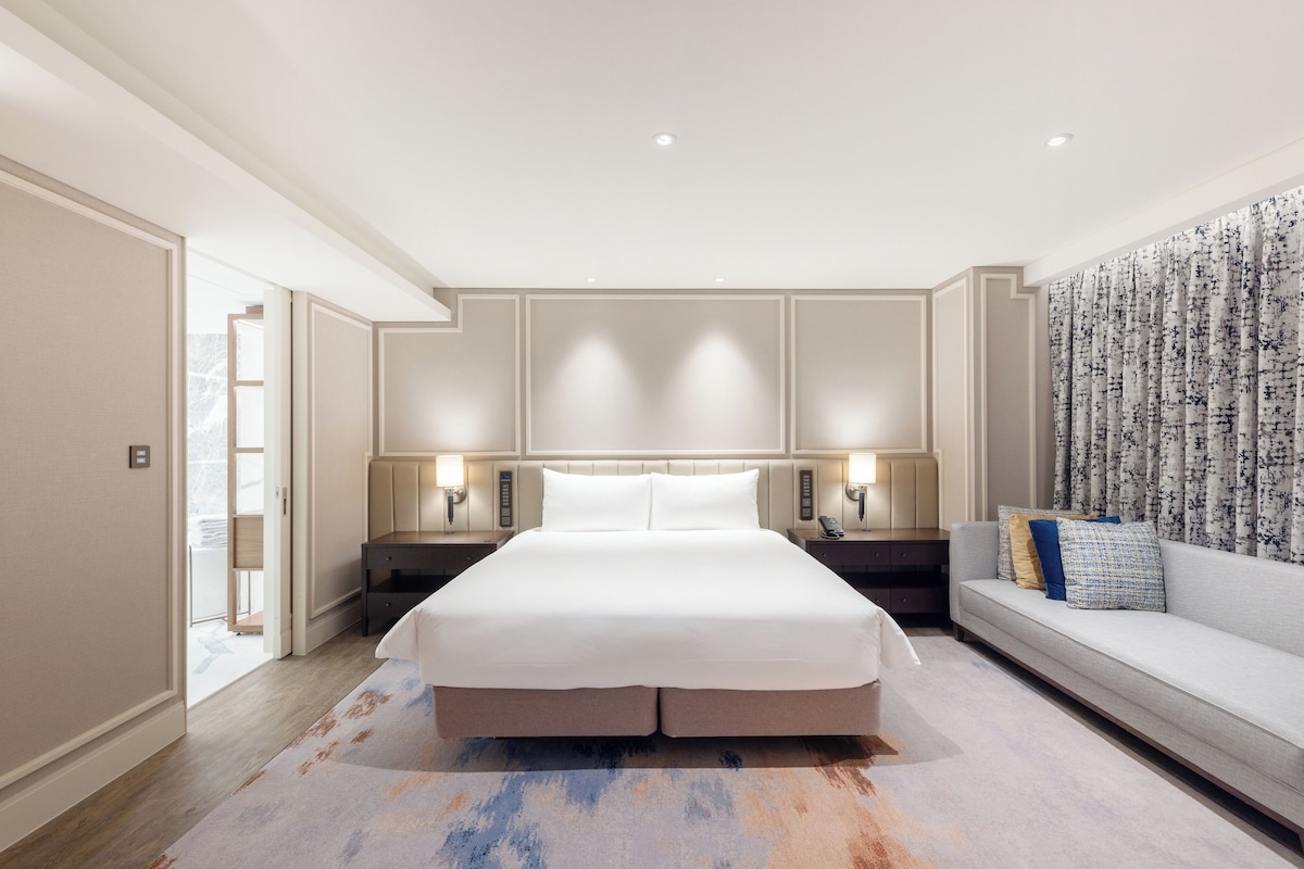 A spacious bedroom with a large bed, bedside lamps, a sofa, and a patterned wall.