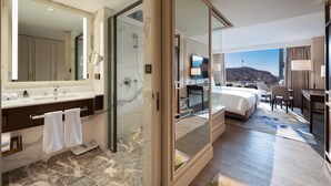 Habitación de hotel moderna con baño de mármol, cama grande, escritorio y vistas a la ciudad.