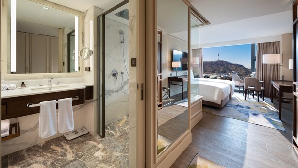 Habitación de hotel moderna con baño de mármol, cama grande, escritorio y vistas a la ciudad.