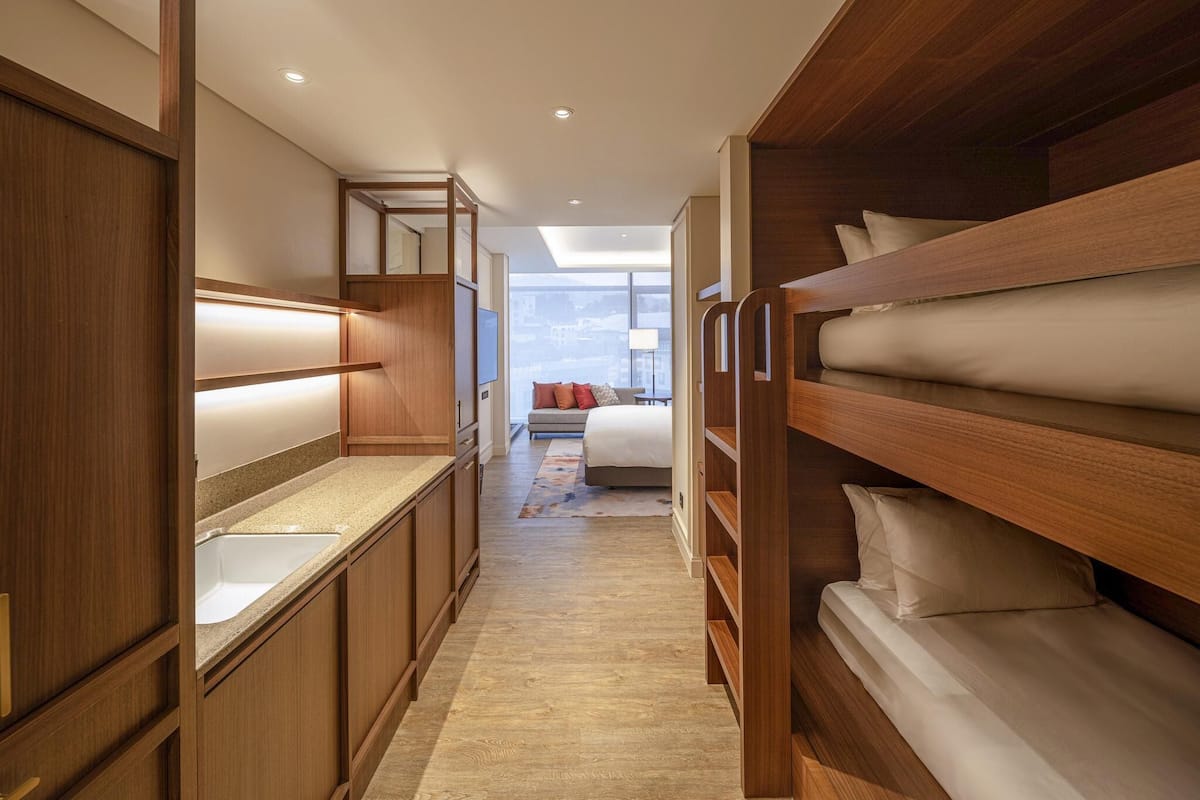 A narrow hallway with wooden bunk beds on one side and a kitchenette on the other.