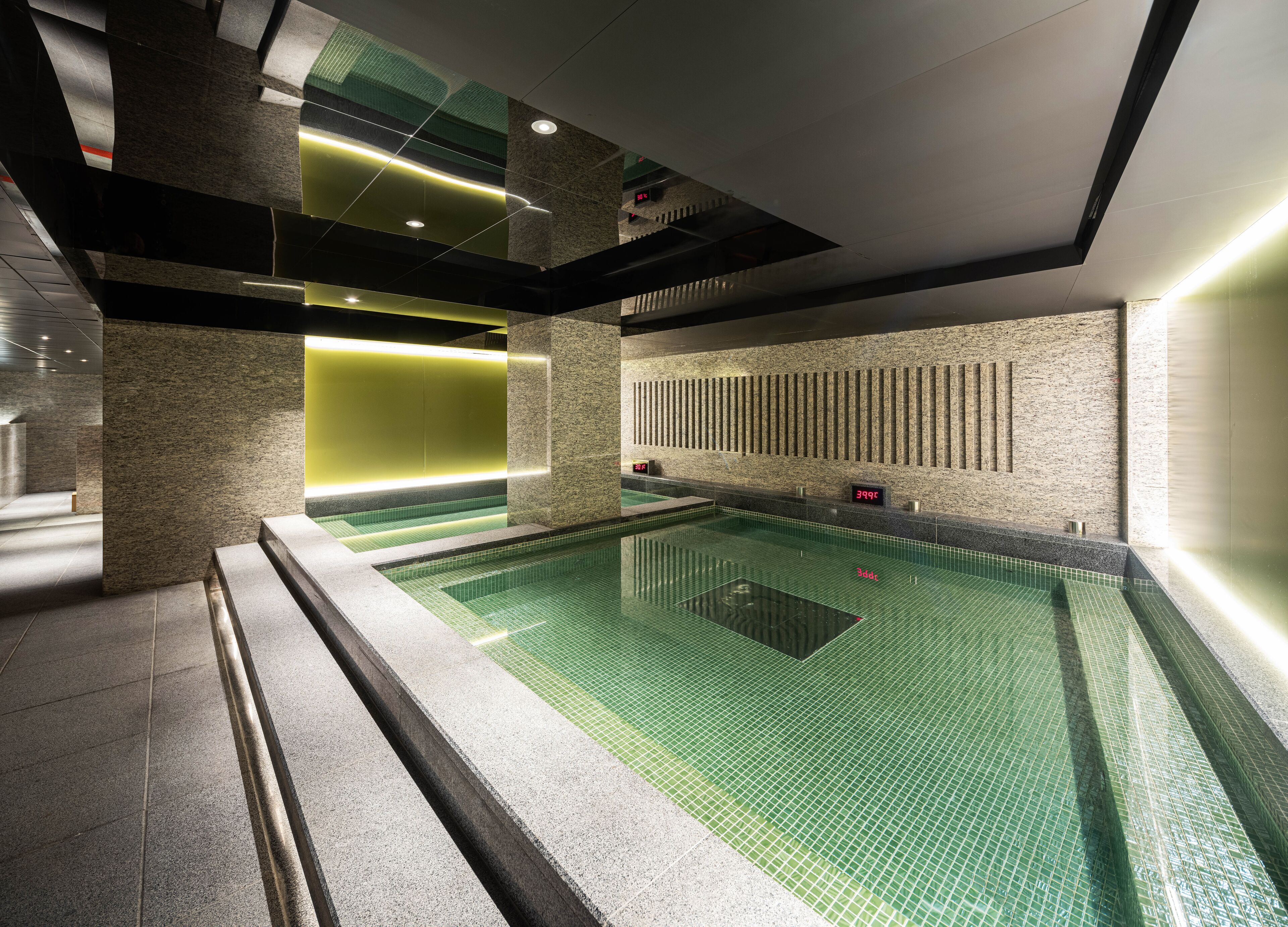 En moderne indendørs swimmingpool med flisegulv, et digitalt termometer og en væg med lodrette linjer.