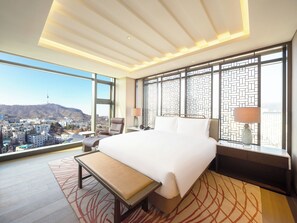 Relax in a stylish room with a large bed, a bench at its foot, and a bedside table with a lamp, offering a city view through large windows.
