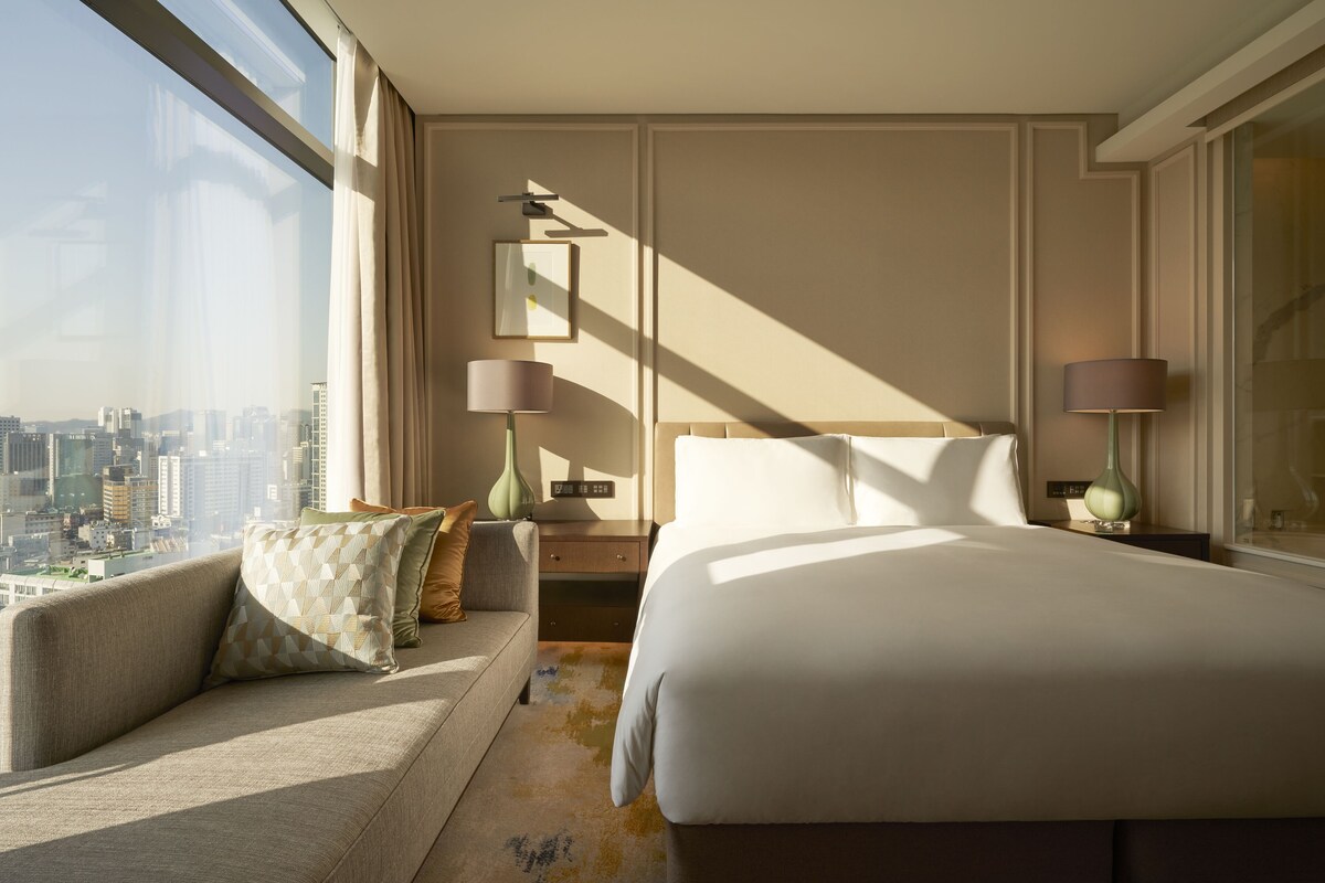 A hotel room with a large bed, a sofa, and a view of a cityscape.