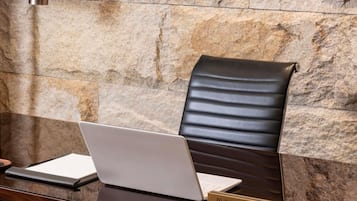 A business center with a laptop on a desk, a leather chair, and a stone wall in the background.